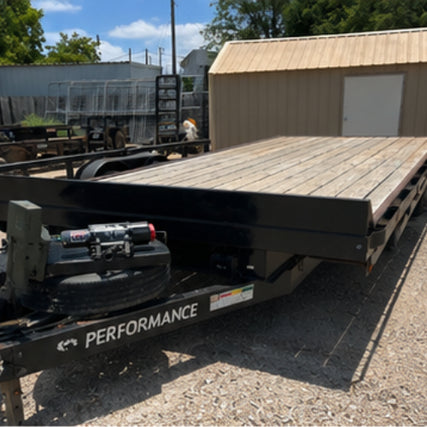TrailersA flatbed trailer with a wooden deck is parked on gravel near a tan metal shed. The word 