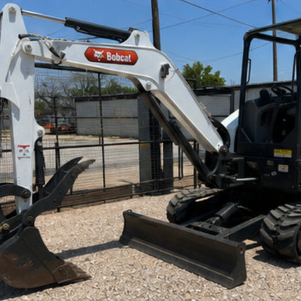 EarthmovingA compact white Bobcat excavator is parked on gravel in a sunlit outdoor setting. The machine features a large digging arm and visible treads.