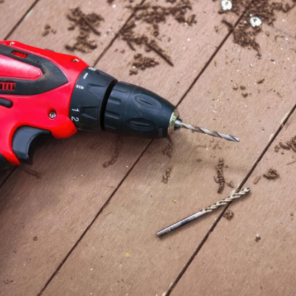 Power ToolsA red electric drill with a drill bit lies on a wooden surface, surrounded by wood shavings and two screws, suggesting recent drilling activity.